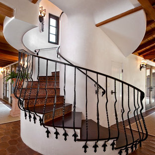 This is an example of a mediterranean wood curved metal railing staircase in Santa Barbara with terracotta risers.