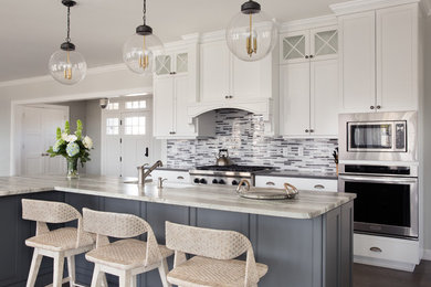 This is an example of a large beach style open plan kitchen in New York with a farmhouse sink, white cabinets, grey splashback, matchstick tile splashback, stainless steel appliances, dark hardwood floors, with island, brown floor and recessed-panel cabinets.
