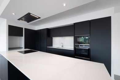 Modelo de cocina abierta con fregadero bajoencimera, puertas de armario negras, encimera de mármol, una isla y encimeras blancas