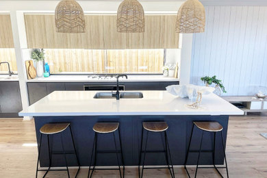 Photo of a large beach style galley open plan kitchen in Geelong with an undermount sink, light wood cabinets, quartz benchtops, window splashback, stainless steel appliances, vinyl floors, with island and white benchtop.