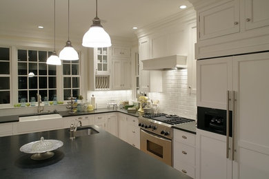 Eat-in kitchen - large traditional l-shaped light wood floor and brown floor eat-in kitchen idea in New York with a farmhouse sink, shaker cabinets, white cabinets, granite countertops, white backsplash, subway tile backsplash, stainless steel appliances and an island