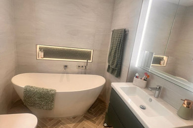 This is an example of a medium sized modern bathroom in Surrey with a corner shower, a wall mounted toilet, grey tiles, grey walls, an integrated sink, brown floors, a hinged door, a single sink and a floating vanity unit.