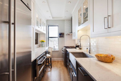 Inspiration for a transitional light wood floor enclosed kitchen remodel in New York with a farmhouse sink, shaker cabinets, white cabinets, quartz countertops, white backsplash and stainless steel appliances