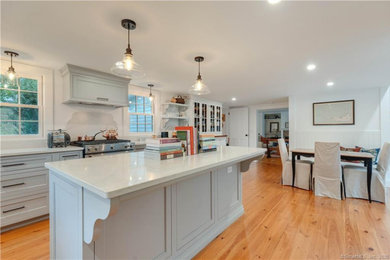 Traditional l-shaped eat-in kitchen in Bridgeport with a farmhouse sink, recessed-panel cabinets, grey cabinets, quartz benchtops, engineered quartz splashback, stainless steel appliances, medium hardwood floors and with island.