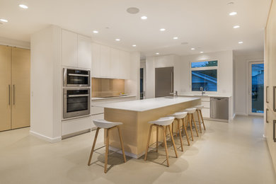 This is an example of a large modern u-shaped eat-in kitchen in Vancouver with solid surface benchtops, with island, an undermount sink, flat-panel cabinets, white cabinets, stainless steel appliances, concrete floors and beige floor.