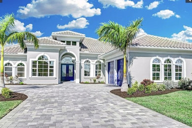 Large one-storey stucco grey house exterior in Miami with a gable roof and a tile roof.