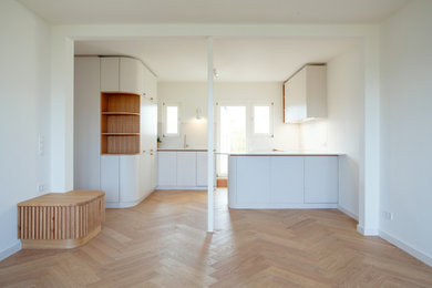 Ejemplo de cocinas en L minimalista con armarios con paneles lisos, puertas de armario blancas, encimera de cuarzo compacto, salpicadero blanco, una isla y encimeras blancas