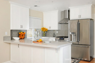 Example of a small minimalist u-shaped medium tone wood floor eat-in kitchen design in San Francisco with a farmhouse sink, shaker cabinets, white cabinets, quartz countertops, gray backsplash, glass tile backsplash, stainless steel appliances and a peninsula