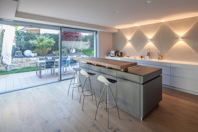 Offene, Zweizeilige, Große Moderne Küche mit integriertem Waschbecken, flächenbündigen Schrankfronten, weißen Schränken, Arbeitsplatte aus Holz, Küchenrückwand in Grau, Rückwand aus Schiefer, Küchengeräten aus Edelstahl, hellem Holzboden, Kücheninsel und braunem Boden in München