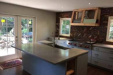 Inspiration for a large classic l-shaped kitchen in Birmingham with a belfast sink, flat-panel cabinets, grey cabinets, concrete worktops, red splashback, brick splashback, stainless steel appliances, dark hardwood flooring, an island and brown floors.