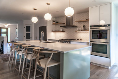 Example of a trendy kitchen design in Other with flat-panel cabinets, white cabinets, quartzite countertops, white backsplash, ceramic backsplash, stainless steel appliances, an island and white countertops
