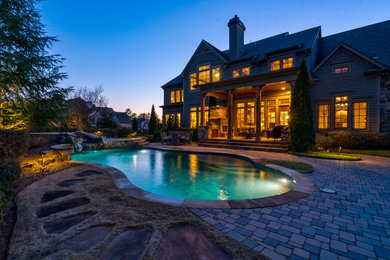 Large classic back custom shaped natural swimming pool in Atlanta with with pool landscaping and concrete paving.