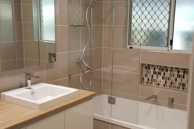 This is an example of a mid-sized modern master bathroom in Brisbane with furniture-like cabinets, white cabinets, a drop-in tub, a corner shower, beige tile, cement tile, a vessel sink, wood benchtops and a hinged shower door.