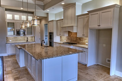 Open concept kitchen - large traditional l-shaped travertine floor and beige floor open concept kitchen idea in Dallas with an undermount sink, recessed-panel cabinets, white cabinets, granite countertops, multicolored backsplash, mosaic tile backsplash, stainless steel appliances and an island