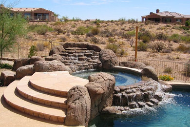 Example of a classic backyard stone and round hot tub design in Phoenix