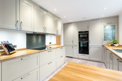 Mid-sized traditional eat-in kitchen in Buckinghamshire with a double-bowl sink, shaker cabinets, grey cabinets, wood benchtops, glass sheet splashback, stainless steel appliances and travertine floors.