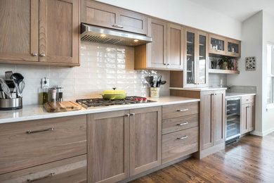 Example of a large trendy galley medium tone wood floor open concept kitchen design in Boise with an undermount sink, shaker cabinets, light wood cabinets, quartz countertops, beige backsplash, subway tile backsplash, stainless steel appliances, a peninsula and white countertops