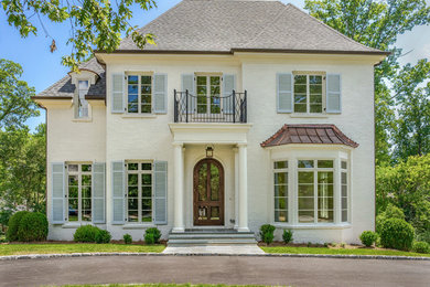 This is an example of a large transitional three-storey brick white house exterior in Raleigh with a clipped gable roof and a shingle roof.