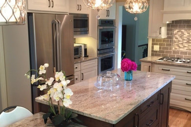 Example of a mid-sized transitional l-shaped light wood floor eat-in kitchen design in Detroit with raised-panel cabinets, white cabinets, granite countertops, beige backsplash, subway tile backsplash, stainless steel appliances and an island
