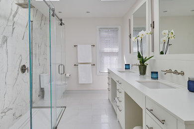 This is an example of a mid-sized modern master bathroom in DC Metro with flat-panel cabinets, white cabinets, a curbless shower, white tile, marble, white walls, porcelain floors, an undermount sink, engineered quartz benchtops, white floor, a sliding shower screen and white benchtops.