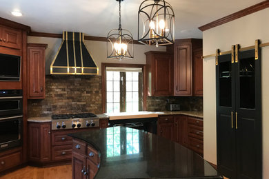 Example of a large classic u-shaped medium tone wood floor and brown floor kitchen design in Other with a double-bowl sink, raised-panel cabinets, medium tone wood cabinets, granite countertops, gray backsplash, stone tile backsplash, stainless steel appliances, an island and white countertops