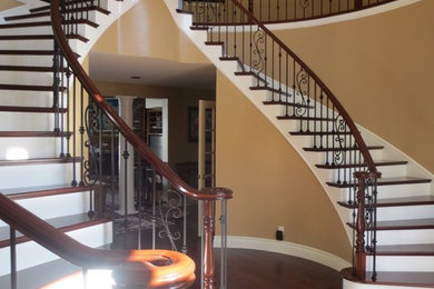 Large elegant wooden curved mixed material railing staircase photo in Orange County with painted risers