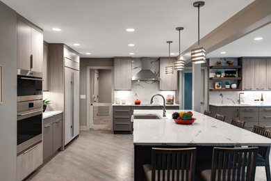 Inspiration for an expansive u-shaped kitchen/diner in Minneapolis with a belfast sink, flat-panel cabinets, light wood cabinets, engineered stone countertops, white splashback, engineered quartz splashback, stainless steel appliances, light hardwood flooring, an island, brown floors and white worktops.