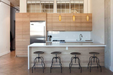Photo of a mid-sized industrial galley open plan kitchen in San Francisco with flat-panel cabinets, medium wood cabinets, white splashback, stainless steel appliances, concrete floors and a peninsula.