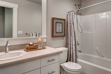 This is an example of a mid-sized traditional 3/4 bathroom in Seattle with flat-panel cabinets, white cabinets, a drop-in tub, an alcove shower, a one-piece toilet, beige tile, glass tile, grey walls, limestone floors, a drop-in sink and limestone benchtops.