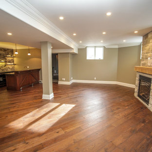 Ejemplo de sótano con ventanas tradicional renovado, grande, con paredes beige, suelo de madera en tonos medios, chimenea tradicional, marco de chimenea de hormigón y suelo marrón