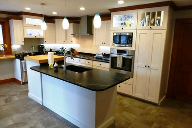 Example of a mid-sized transitional l-shaped ceramic tile kitchen design in Burlington with an undermount sink, flat-panel cabinets, light wood cabinets, soapstone countertops, stainless steel appliances and an island