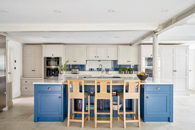 This is an example of a large contemporary l-shaped open plan kitchen in Other with a farmhouse sink, shaker cabinets, blue cabinets, blue splashback, glass sheet splashback, stainless steel appliances, with island, beige floor, white benchtop, quartzite benchtops and limestone floors.