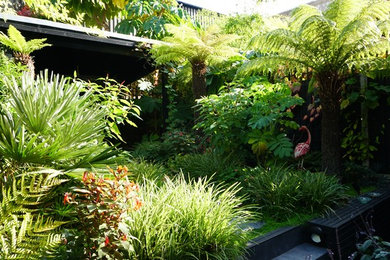 This is an example of a small world-inspired back partial sun garden for summer in London with a retaining wall and natural stone paving.