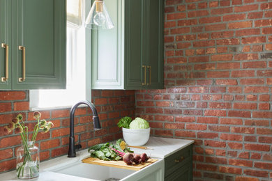 Example of a small classic medium tone wood floor enclosed kitchen design in Other with a farmhouse sink, recessed-panel cabinets, green cabinets, marble countertops, red backsplash, brick backsplash, paneled appliances and white countertops