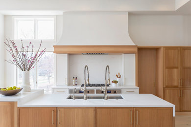 Inspiration for a large transitional single-wall open plan kitchen in Minneapolis with an undermount sink, flat-panel cabinets, white cabinets, quartz benchtops, white splashback, engineered quartz splashback, stainless steel appliances, light hardwood floors, multiple islands, brown floor and white benchtop.