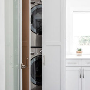 バンクーバーの中サイズのコンテンポラリースタイルのおしゃれな洗濯室 (白いキャビネット、白い壁、上下配置の洗濯機・乾燥機、黒い床、白いキッチンカウンター、落し込みパネル扉のキャビネット、クオーツストーンカウンター、大理石の床) の写真