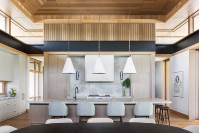 Large island style l-shaped medium tone wood floor, brown floor, vaulted ceiling and wood ceiling open concept kitchen photo in Hawaii with flat-panel cabinets, marble countertops, marble backsplash, an island, light wood cabinets, gray backsplash, paneled appliances and gray countertops