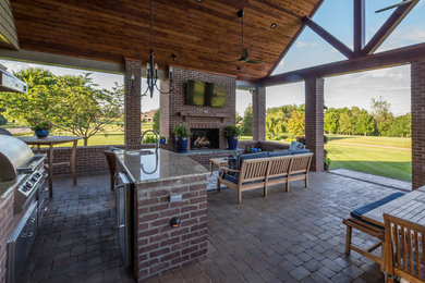 This is an example of a large country backyard patio in Other with an outdoor kitchen, concrete pavers and a roof extension.