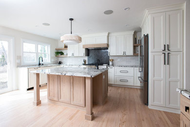 Transitional u-shaped light wood floor and beige floor kitchen photo in Chicago with an undermount sink, shaker cabinets, medium tone wood cabinets, granite countertops, white backsplash, ceramic backsplash, stainless steel appliances, an island and multicolored countertops