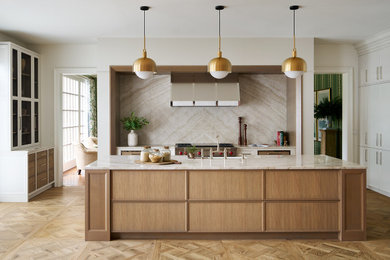 Huge transitional light wood floor and brown floor kitchen photo in Chicago with a farmhouse sink, recessed-panel cabinets, light wood cabinets, quartzite countertops, beige backsplash, mirror backsplash, stainless steel appliances, an island and beige countertops