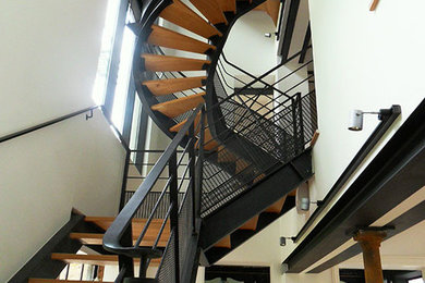 Идея дизайна: большая изогнутая лестница в стиле модернизм с деревянными ступенями и металлическими перилами без подступенок