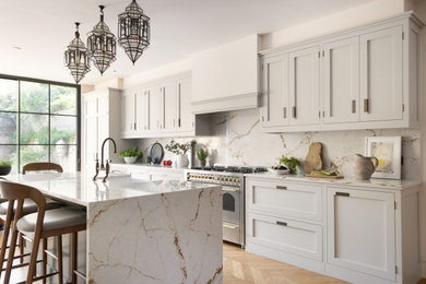 Large traditional galley kitchen/diner in London with a belfast sink, shaker cabinets, quartz worktops, engineered quartz splashback, stainless steel appliances, medium hardwood flooring and an island.