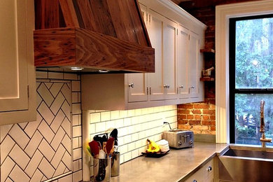 Small farmhouse galley medium tone wood floor kitchen photo in New York with a farmhouse sink, shaker cabinets, white cabinets, concrete countertops, white backsplash, subway tile backsplash and stainless steel appliances