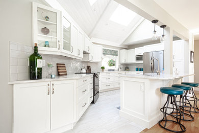Example of a mid-sized classic u-shaped laminate floor and beige floor eat-in kitchen design in Vancouver with a farmhouse sink, shaker cabinets, white cabinets, quartz countertops, gray backsplash, ceramic backsplash, stainless steel appliances, an island and white countertops