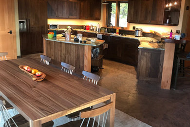 Eat-in kitchen - mid-sized craftsman u-shaped concrete floor, brown floor and exposed beam eat-in kitchen idea in Salt Lake City with a farmhouse sink, recessed-panel cabinets, dark wood cabinets, granite countertops, brown backsplash, wood backsplash, stainless steel appliances, an island and multicolored countertops
