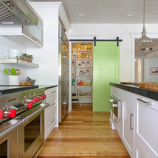 Réalisation d'une grande arrière-cuisine champêtre en L avec un placard avec porte à panneau encastré, une façade en inox, un plan de travail en granite, une crédence blanche, une crédence en carreau de porcelaine, un sol en bois brun, un îlot central, un évier encastré et un électroménager en acier inoxydable.