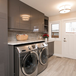 Modelo de cuarto de lavado lineal, clásico renovado, de tamaño medio, con armarios con paneles lisos, puertas de armario grises, paredes beige, lavadora y secadora juntas, fregadero bajoencimera, encimera de cuarzo compacto, suelo de baldosas de porcelana, suelo gris y encimeras beige