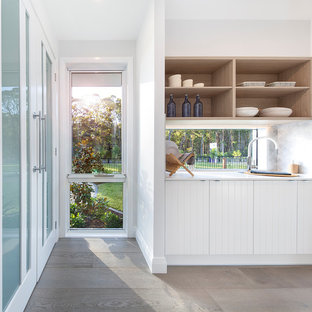 Inspiration for a large beach style galley kitchen pantry in Sydney with a drop-in sink, shaker cabinets, white cabinets, solid surface benchtops, glass sheet splashback, white appliances, cement tiles, multiple islands, grey floor and white benchtop.