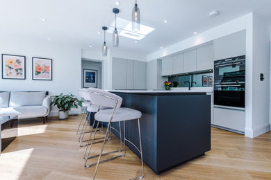 Inspiration for a large modern kitchen in Manchester with an integrated sink, flat-panel cabinets, quartz worktops, metallic splashback, glass sheet splashback, stainless steel appliances and an island.