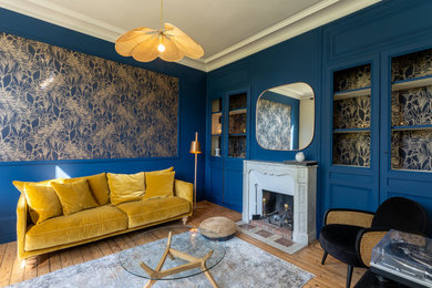 Idée de décoration pour un salon vintage de taille moyenne et fermé avec un mur bleu, parquet clair, une cheminée, un manteau de cheminée en pierre, un téléviseur indépendant et du papier peint.